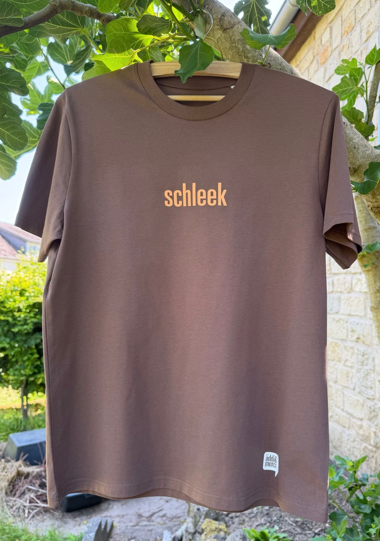 Brown t-shirt with 'schleek' logo on a hanger outdoors.